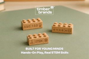 Three Timber Brands wooden building bricks engraved with letters, numbers, math symbols, and "STEM" on a green surface, beneath the words "Built for Young Minds."