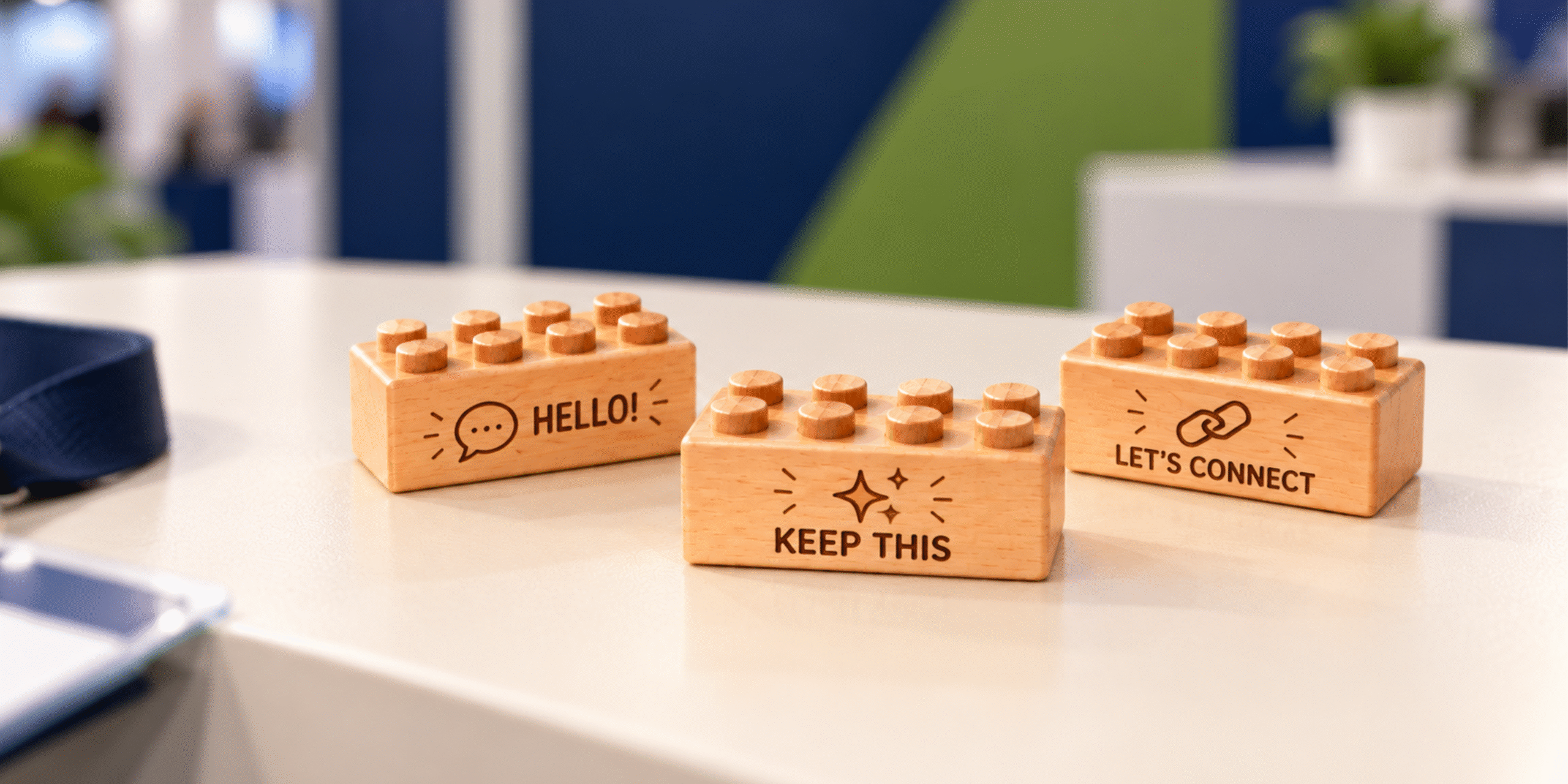 Three wooden giveaway bricks engraved with Hello, Keep This, and Let's Connect on a trade show table.