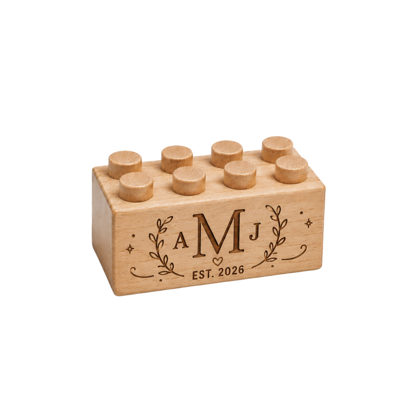 Wooden wedding brick engraved with an A M J monogram and Est. 2026, framed by leafy branches and a heart.